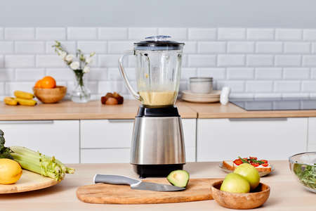 Modern electric blender with fresh cocktail inside standing on table among fruits and vegetables