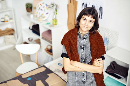 Portrait of smiling creative young fashion designer standing in her studio and looking at camera