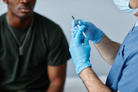 Doctor wearing protective mask and gloves preparing syringe removing extra air out of it to...