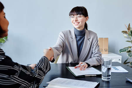 Portrait of smiling young businesswoman shaking hands with female partner as greeting during meeting...