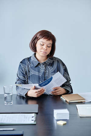 Minimal portrait of young African American woman with short haircut reading documents at workplace...