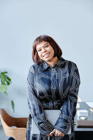 Minimal portrait of young black woman with short haircut smiling at camera cheerfully while standing...