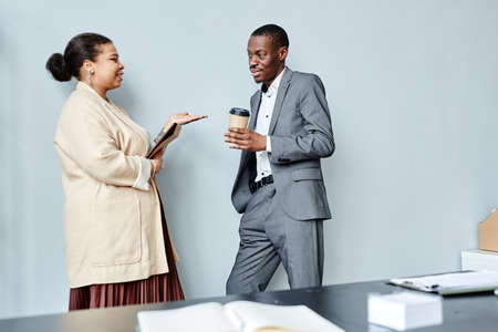 Minimal side view portrait of two African American business people chatting casually while leaning...