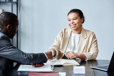 Portrait of smiling African American businesswoman shaking hands with client or partner during...
