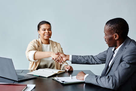 Minimal portrait of smiling African American businesswoman shaking hands with partner or client...