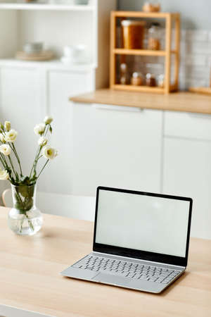 Vertical background image of white laptop screen on wooden table in kitchen decorated with fresh flowers in Spring, copy spaceの写真素材