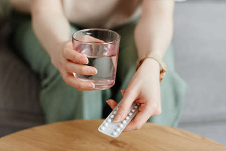 Close up of unrecognizable woman taking birth control pills with glass of waterの写真素材