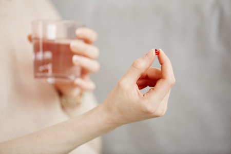 Minimal close up of young woman holding pill capsule and glass of water while taking medicine or vitamins, copy spaceの写真素材