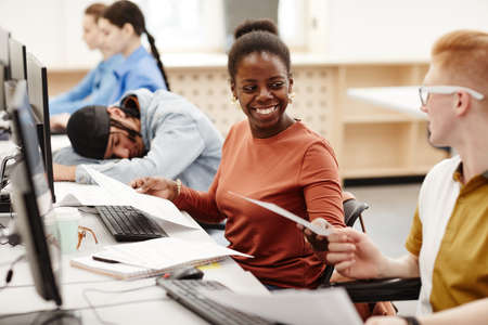 Vibrant portrait of smiling African American woman handing notes to friend in class while studying...