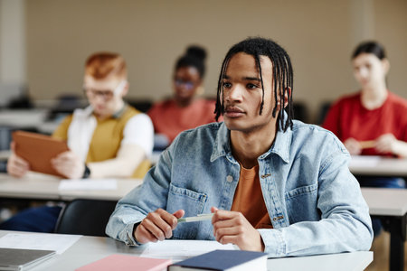 Portrait of black teenage boy with braids listening to lecture in school or college, copy spaceの写真素材