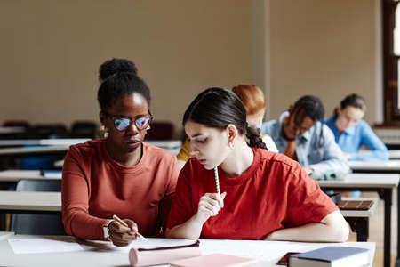 Front view portrait of two young women taking notes while studying in college classroom, copy spaceの写真素材
