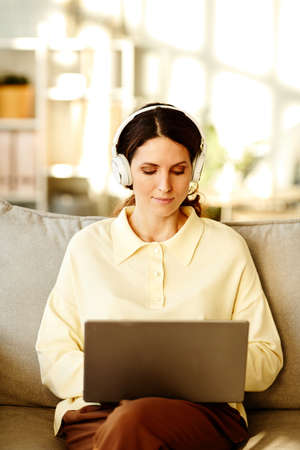Vertical shot of beautiful young adult Caucasian woman wearing casual clothes and headphones sitting...