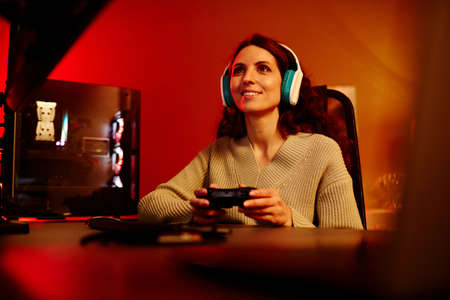 Modern young adult Caucasian woman playing racing or shooter video game using console in living room...