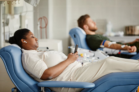 Side view portrait of two people giving blood and lying in chairs at donation center, copy spaceの写真素材