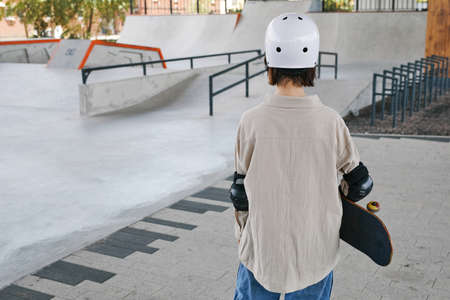 Minimal back view of young girl wearing protective guards and helmet in skating park outdoors, copy...