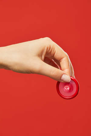 Vibrant closeup of female hand holding condom against red background safe sex and protection conceptの写真素材