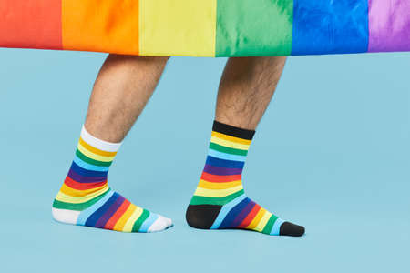 Close up shot of couple wearing rainbow socks with LGBTQ flag on pastel blue background