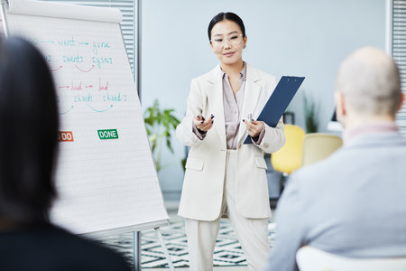 Portrait of young Asian woman giving English lesson in office and speaking to audience by whiteboardの写真素材