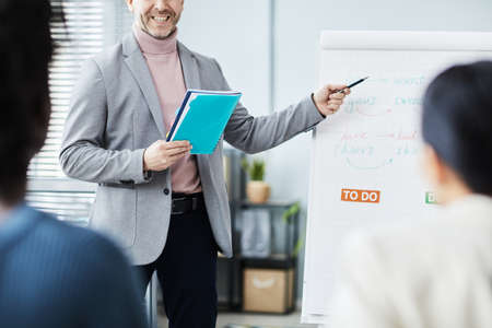 Cropped portrait of mature man giving English lessons in office to group of people and pointing at...