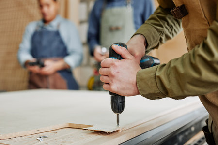 Close up of male carpenter drilling wood while building handmade furniture in workshop, copy spaceの写真素材