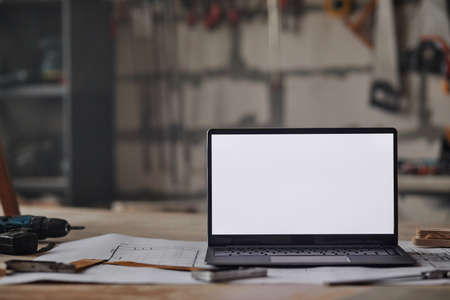 Close up background image of opened laptop with blank white screen on table in workshop, copy spaceの写真素材