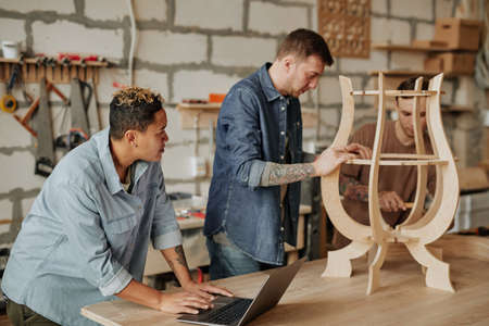 Warm toned portrait of two modern carpenters designing wooden furniture in workshop interiorの写真素材