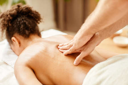 Close up of male hands massaging back of young African American woman enjoying SPA sessionの写真素材