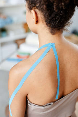 Vertical closeup of young woman with physio tape on shoulder in rehabilitation therapyの写真素材