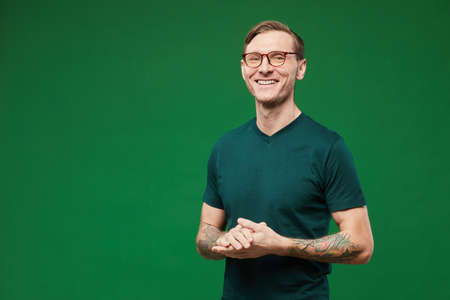 Waist up portrait of tattooed man wearing green shirt and glasses against vibrant green background in studio and smiling at camera, copy spaceの写真素材