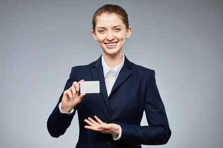 Waist up portrait of smiling young businesswoman holding blank credit card mockup and showing to camera with grey background, copy spaceの写真素材