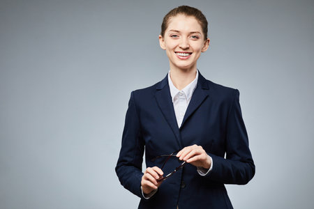 Waist up portrait of young businesswoman smiling to camera and holding glasses in hand, copy space