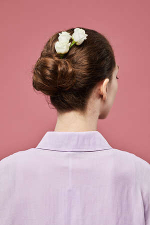 Minimal back view of young woman with roses in hair against vibrant pink backgroundの写真素材
