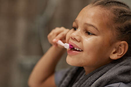 Close up of little black girl brushing teeth with pink toothbrush good dental hygiene practice in childhoodの写真素材