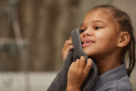 Close up of little black girl washing face in bathroom and holding towel, night or morning hygiene, copy spaceの写真素材