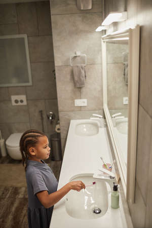 Vertical portrait of little black girl brushing teeth with pink toothbrush by mirror good dental hygiene practice in childhoodの写真素材