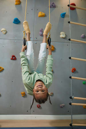 Full length portrait of active black child hanging upside down on sports rings at home and having funの写真素材