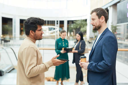 Side view portrait of two businessmen talking while standing in office building settingの写真素材