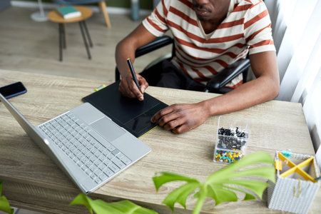 Top view closeup of African American man in wheelchair using pen tablet while working with computer...