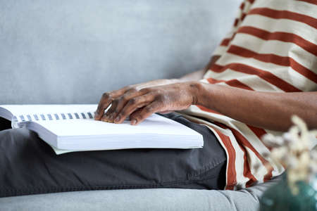 Side view close up of blind man reading book in Braille at home while lying on couch, copy space