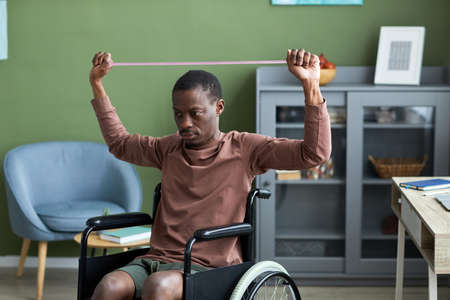Minimal portrait of adult black man with disability exercising at home using elasticsの写真素材