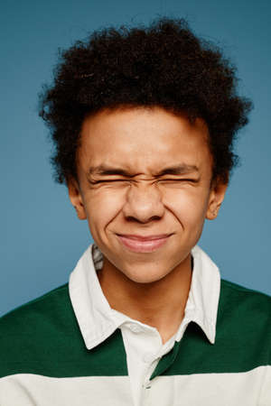 Vertical close up portrait of black teenage boy facing camera with eyes closed and funny expressionの写真素材