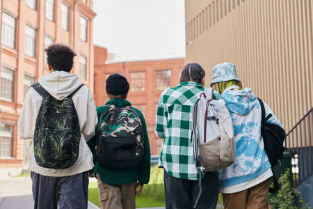 Rear view of group of teenage students with backpacks walking along school yard after classesの写真素材