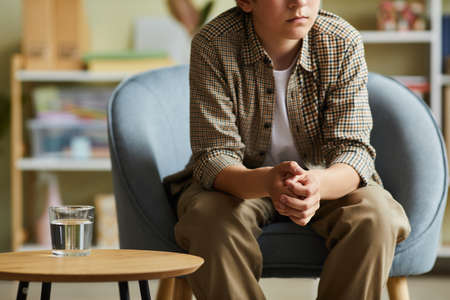 Close-up of teenage boy sitting on armchair at psychotherapist office and having individual sessionの写真素材