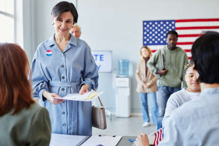 Front view portrait of smiling adult woman receiving ballot at voting station, copy space