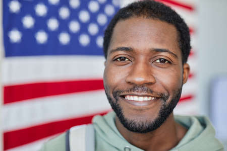 Closeup portrait of smiling black man looking at camera against American flag in background, copy spaceの写真素材