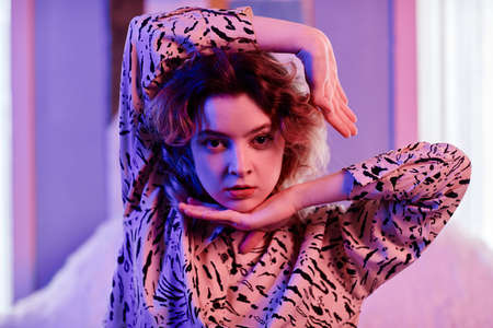 Close up portrait of female vogue dancer looking at camera in neon light with focus on hand...