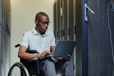 Portrait of African American man with disability using laptop in server room while working as IT technicianの写真素材
