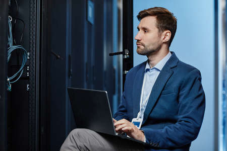 Side view portrait of IT system administrator using laptop in server room, copy space