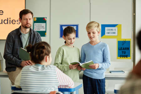 Portrait of two kids answering questions in school in front of classroom, copy spaceの写真素材