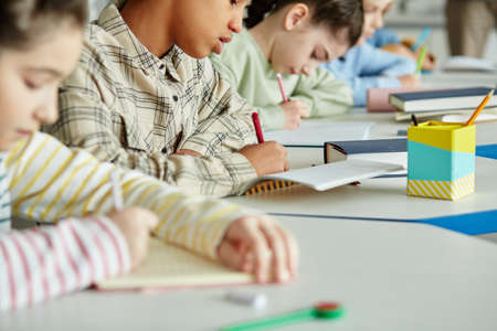 Close up of diverse group of children sitting in row and taking test in school classroomの写真素材
